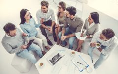 High angle view of business people using gadgets, talking and smiling while working in office