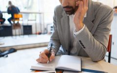 Man writing in notebook while talking on cellphone at work